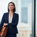 Profesjonalna bizneswoman w granatowej marynarce z teczką stoi w nowoczesnym biurze