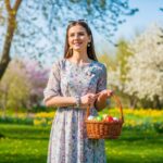 Młoda kobieta w wiosennym ogrodzie z koszem ozdobionych pisanek wielkanocnych