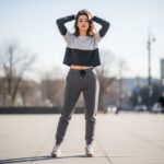 Młoda kobieta w miejskim stylu w dresowych spodniach i sneakersach na tle rozmytego miasta