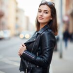 Młoda kobieta w ramonesce stoi pewnie na miejskiej ulicy w casualowym stylu.